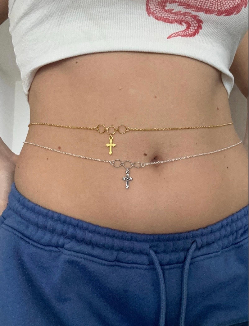 Icegold by Vee cross pendant belly chain featuring a delicate metal chain with a small cross pendant, designed to be worn around the waist.